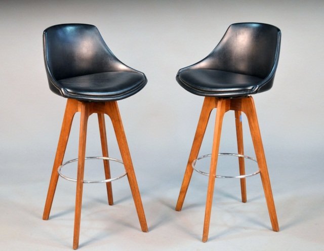 Set of Four Walnut Bar Stools: Circa 1950's, Black vinyl seat on tapered legs joined by a chrome circular footrest. Height 40 inches, width 20 inches, depth 16 inches.