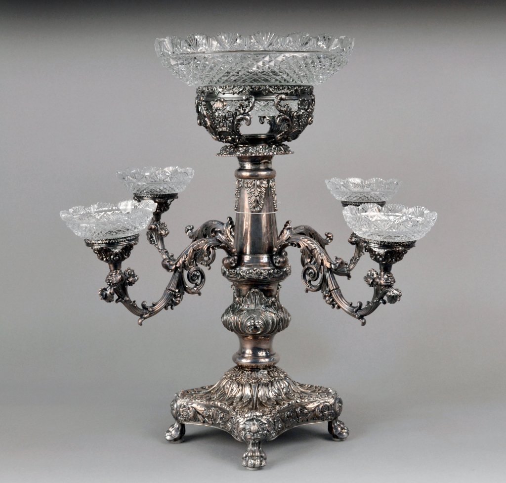 Victorian Silver Plated Epergne: Circa 1840, central glass bowl with fan cut rim and diamond cutting supported on a tapered column issuing for detachable branches with scroll decoration, on a shaped square base on scrolled paw feet.