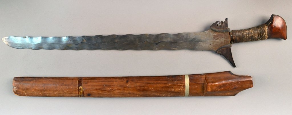 Early Indonesian Balinese Kris: Wavy blade with a metal mounted and cord wrapped wooden handle, with similar wooden scabbard. Blade length 21 3/4 inches.