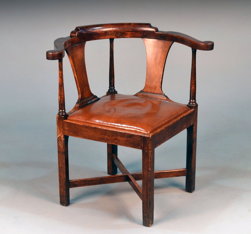 George III Mahogany Corner Chair: 18th century. Of typical form with a tablet crest rail, outscrolled arms, leather slip seat, and square chamfered legs joined by a cross stretcher. Height 31 inches, width 30 inches, depth 26 inches.