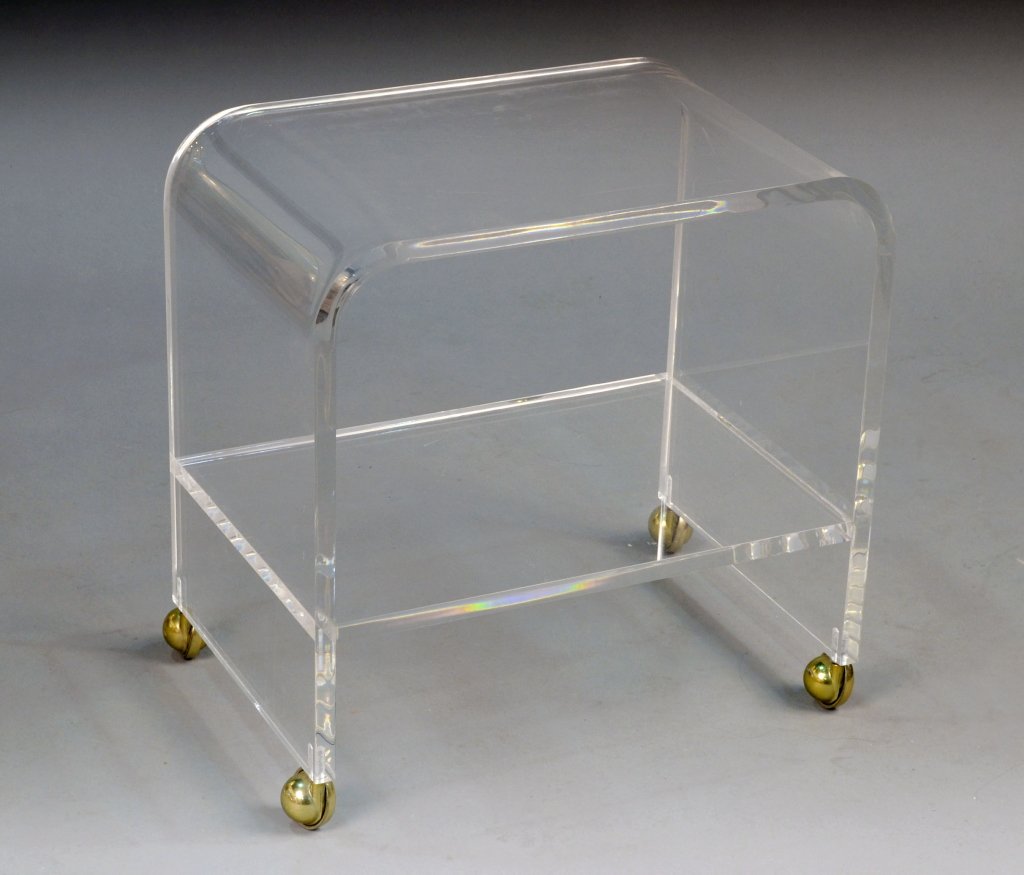 Lucite Two Tier Stand: Rectangular bent top, joined by a lower shelf, on castors. Height 21 inches, width 20 inches, depth 13 inches.