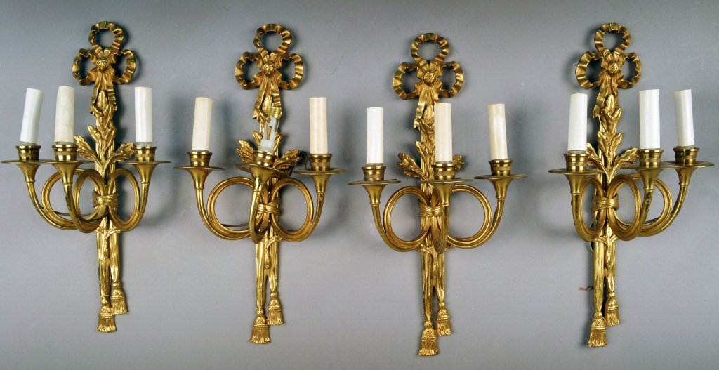 Four Brass Three-Light Sconces: Neoclassical style, with tied bow ribbons and tassels. Height 19 inches.