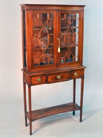 Hepplewhite Style Mahogany Vitrine on Stand: Rectangular top with molded edge above two glazed mullioned doors, the base with central outset drawer flanked by two short drawers, on square tapered legs joined by a shaped rectangular shelf. Height