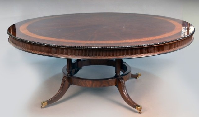 English George III Style Mahogany Dining Table: Circular top with inlaid exotic wood border and beaded edge, above fluted columnar legs joined by a circular stretcher, on brass castors. Height 31 inches, diameter 6 feet 8 inches.