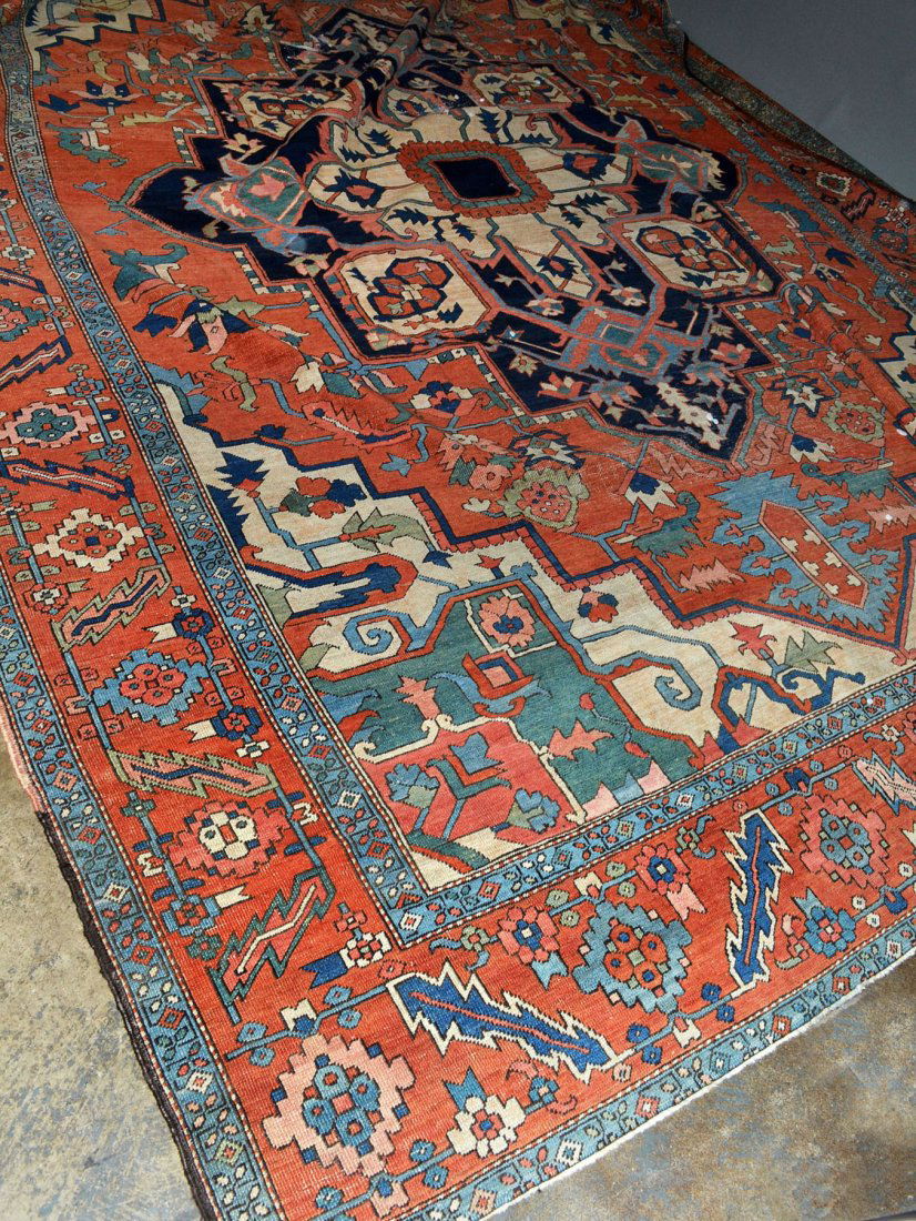 Serapi Carpet: Central medallion on a rust colored field with allover stylized floral and geometric decoration within a blue and rust colored guard border with similar decoration. 9 feet x 11 feet 10 inches.