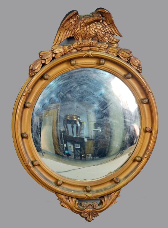 Gilt Wood Convex Mirror: Circular convex plate surrounded by gilt wood frame with gilt wood decoration and eagle pediment. Height 29 inches, width 20 inches.