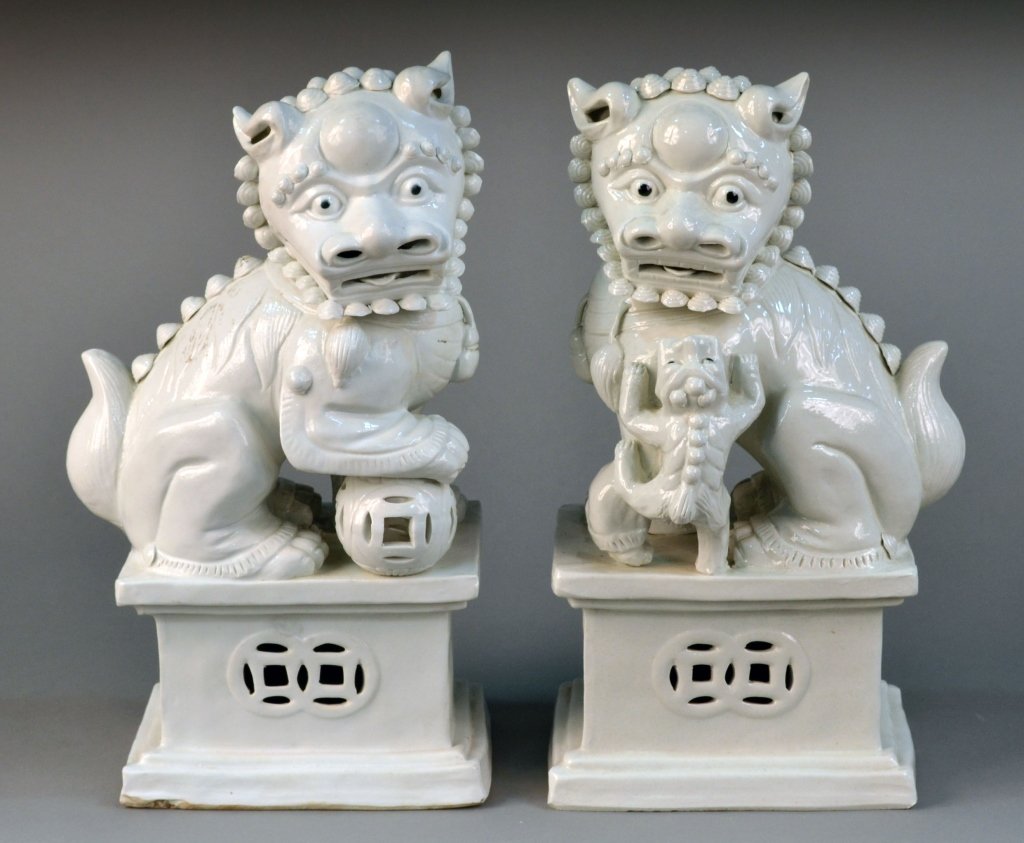 Pair of Blanc de Chine Foo Lions: Modeled with one standing on a ball, the other standing on a cub. Height 15 1/2 inches.