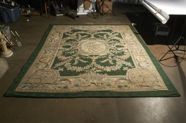 Needlepoint Carpet: Central floral medallion on a green field with a wide guard border with floral basket corner decoration. 9 feet 8 inches x 8 feet 1 inch.