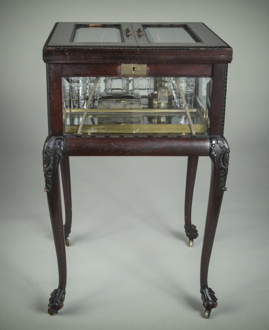 Mahogany Glazed Panel Liqueur Cabinet: Two door lift top opening to a rising decanter set, with two decanters, a set of glasses, humidor and matchbox holder with ashtrays. Height 31 1/2 inches, width 19 inches, depth 19 1/2 inches.