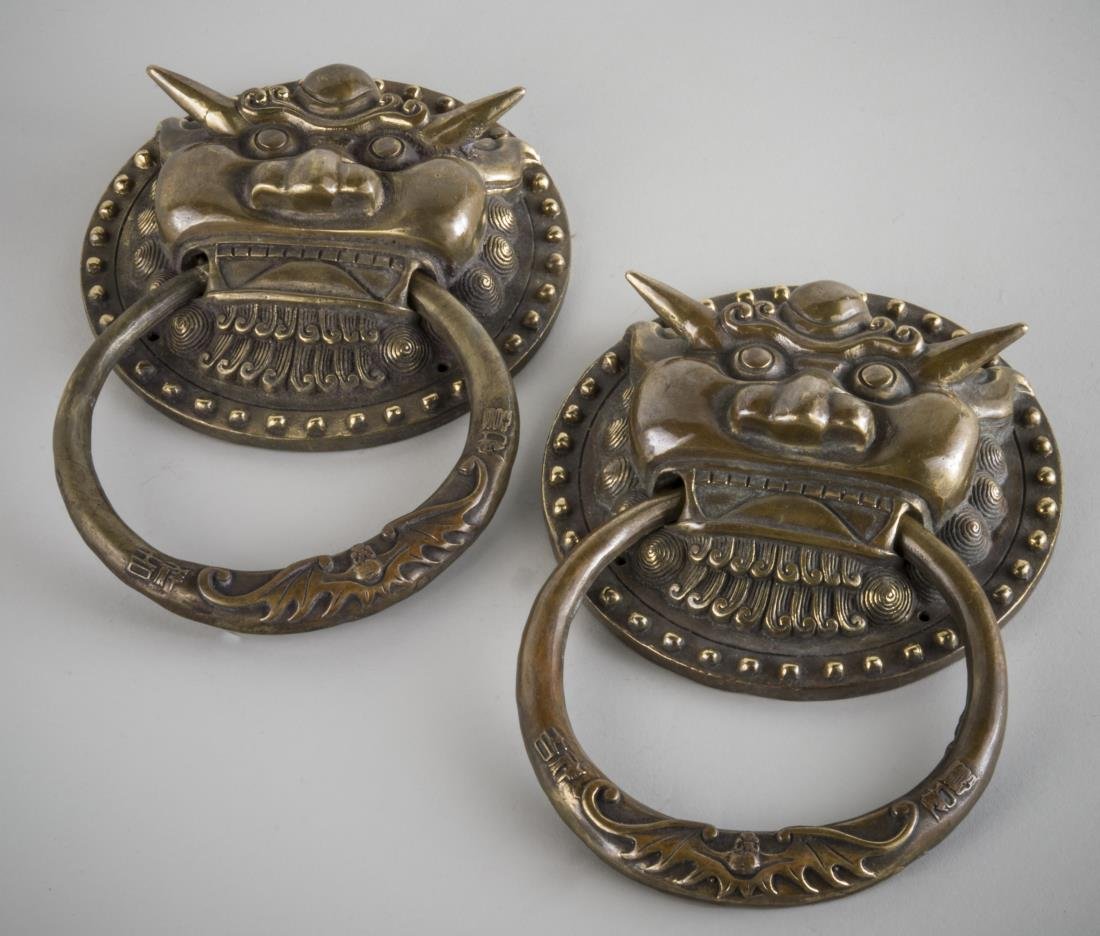 Pair of Chinese Bronze Lion Head Door Knockers: Each with high relief design of a lion with a bat decorated ring in his mouth. Height 9 1/4 inches, width 6 1/4 inches. Provenance: From a Pennsylvania Private Collection.