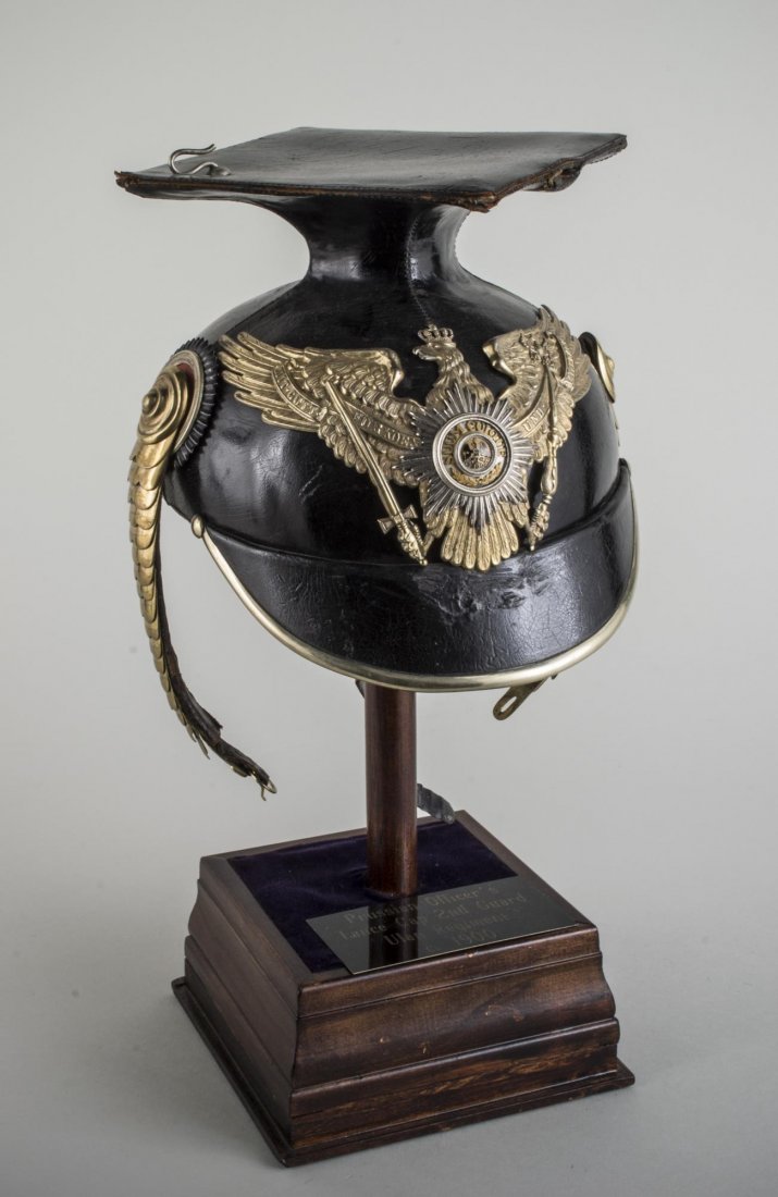 Prussian Officer's Ulan Cavalry Tschapka: Circa 1900, black leather cap with mortarboard, brass fittings and chinstrap,on a stand with placard. Overall height 15 1/2 inches.