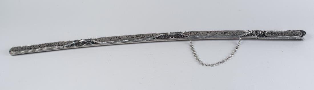 Caucasian Shashka: Kubachi region, the slightly curved single edged blade with double fuller and parade finish, the silvered bifurcated handle and scabbard with enamel scroll and filigree decoration. Blade length 26 inc