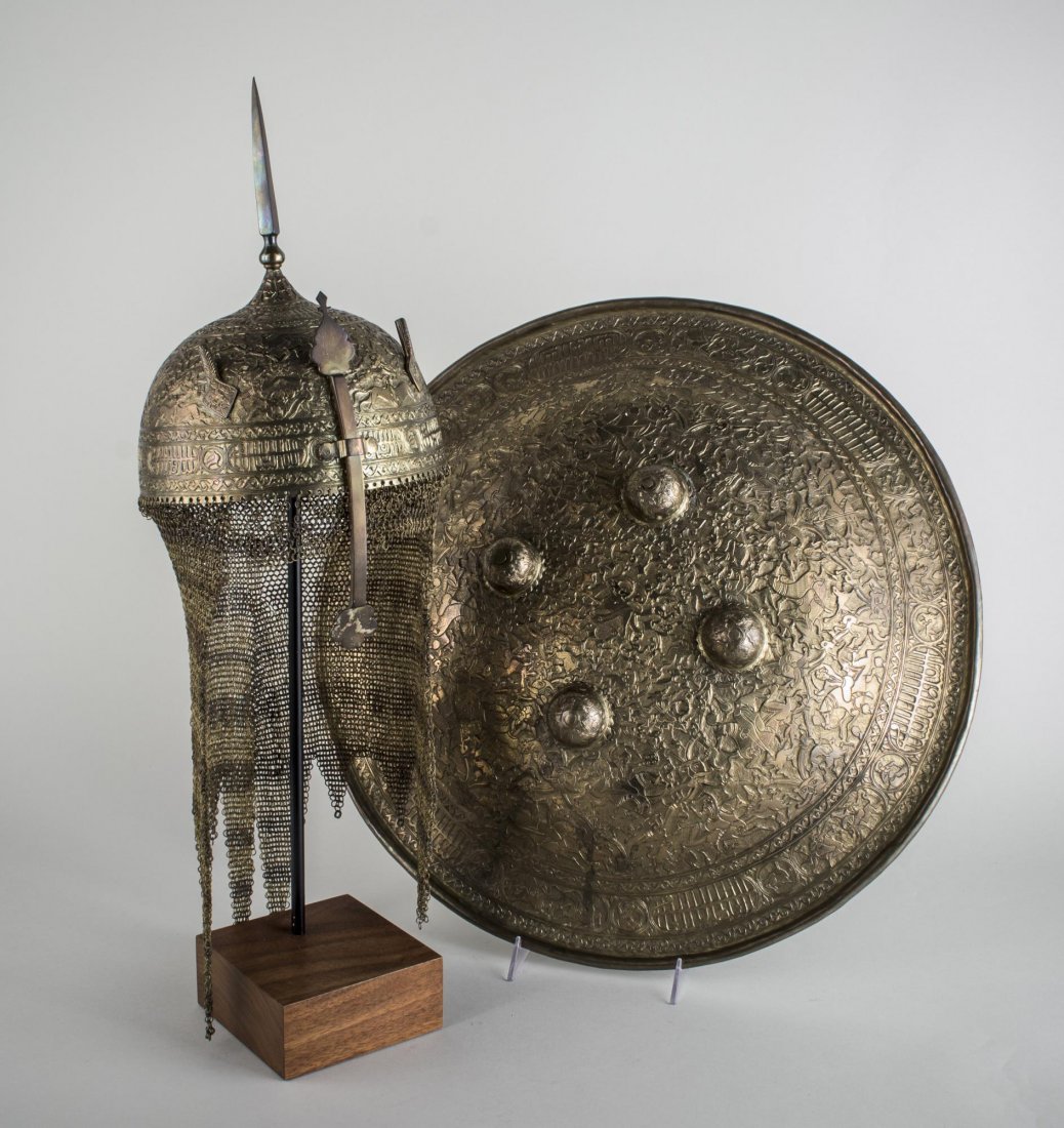 Indo-Persian Kulah Khud Helmet and Dhal Shield: The brass dome shaped helmet with center spike, chain mail neck guard, and adjustable nasal guard all with chased and etched figural and calligraphy decoration, on stand, the matching shield with four