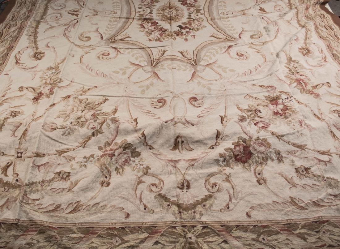 Aubusson Carpet: Central floral medallion on a tan field with floral, acanthus and scroll decoration, all within a guard border with wreath and ribbon decoration. 15 feet x 10 feet.