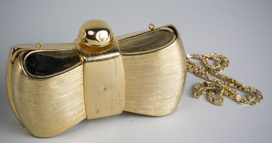 Judith Leiber Gold Tone Purse: In the form of a bow with striated texture, dome form clasp, includes shoulder chain. Measure 3 1/ inches tall, 6 inches wide, 2 inches deep. Notice to bidders: Condition reports and additional photog