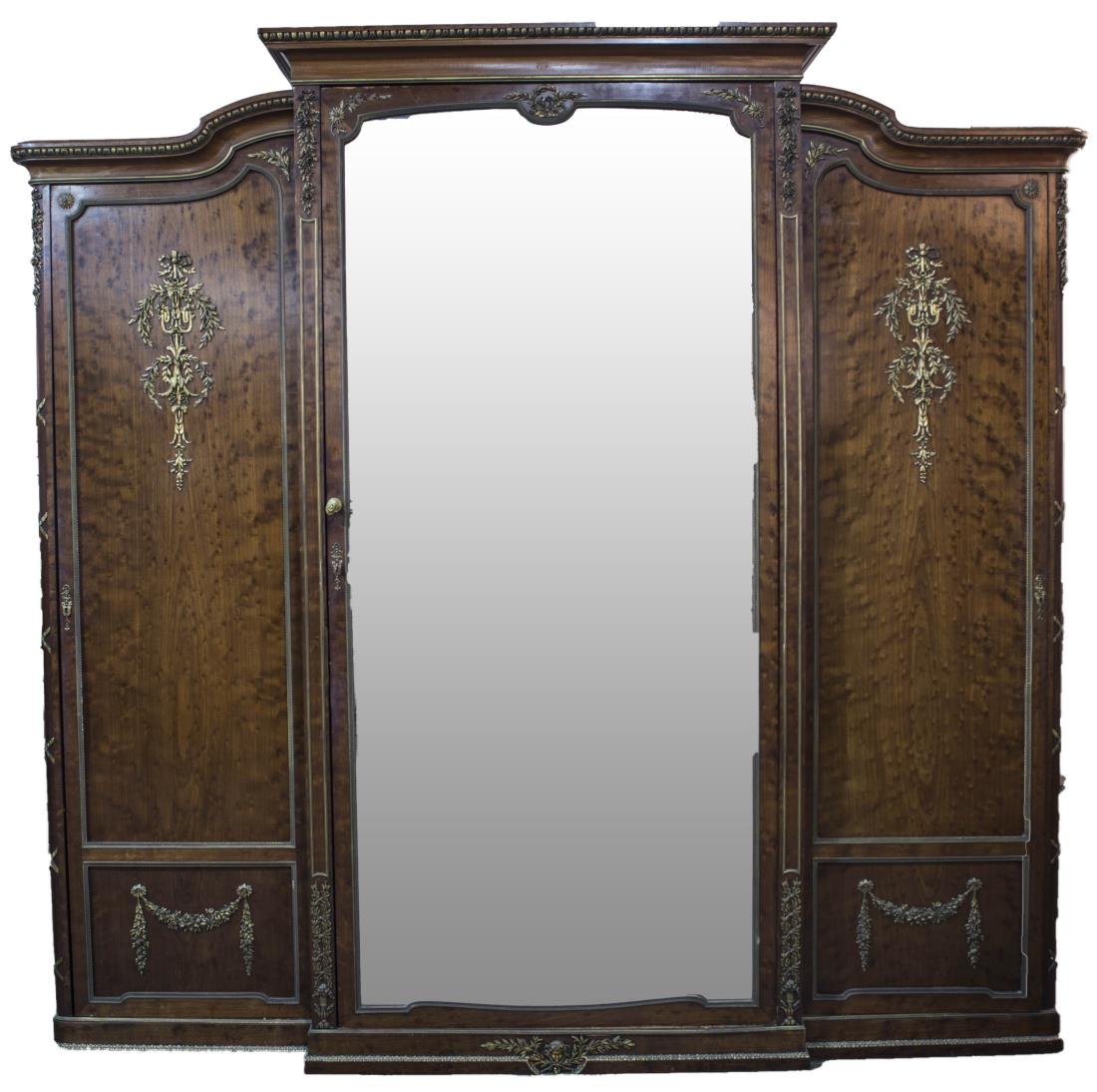 Continental Gilt Metal Mounted Armoire: Neoclassical style, molded cornice over a central mirrored door, flanked by two doors mounted with classical trophies and ribbon tied columns Height 7 feet 6 inches, width 8 feet, depth 24 inches. Not