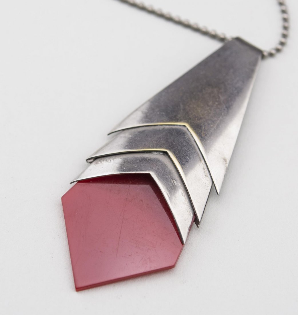 Jakob Bengel Chrome & Red Galalith Necklace: Chrome bead chain suspending a pendant in the form of a necktie. Length 20 inches. Notice to bidders: Condition reports and additional photographs are provided by request as a courtesy to our clients,