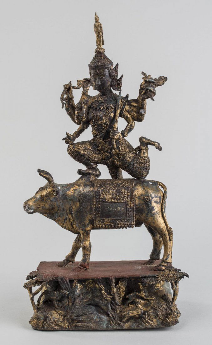 Thai Gilt Metal Deity: 19th century, the ten-armed deity stands upon the back of a bull, all mounted atop a base with forest vignette featuring a tiger in pursuit of prey. Height 14 5/8 inches. Notice to bidders: Condition