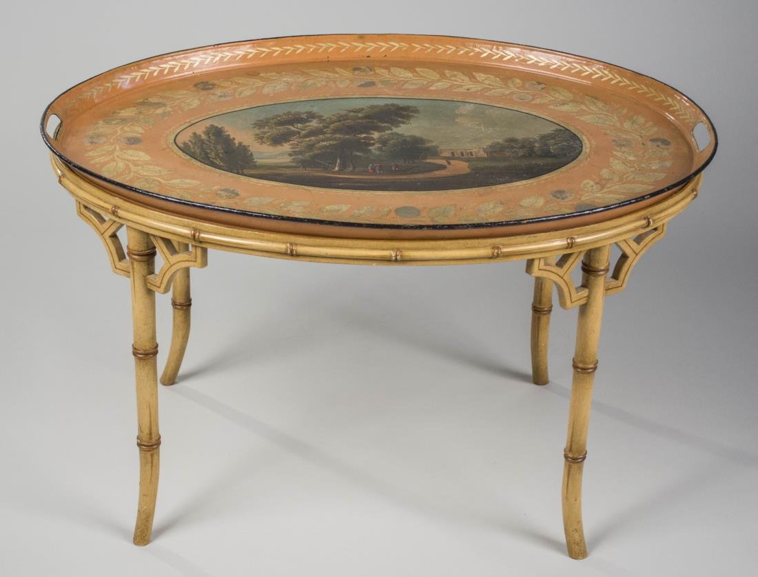 Tole Tray Table: Oval tray painted with a landscape scene with figures, within a laurel leaf border, on a faux bamboo base. Height 18 inches, width 30 inches, depth 22 inches. Notice to bidders: Condition reports and