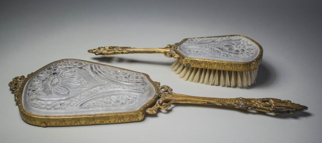 French Gilt Metal and Frosted Glass Dresser Set: Comprising a hand mirror and a hair brush, both with ribbon, scroll and acanthus leaf gilt decoration and each with inset cartouche shaped clear and frosted glass panel with floral decoration. Mirror