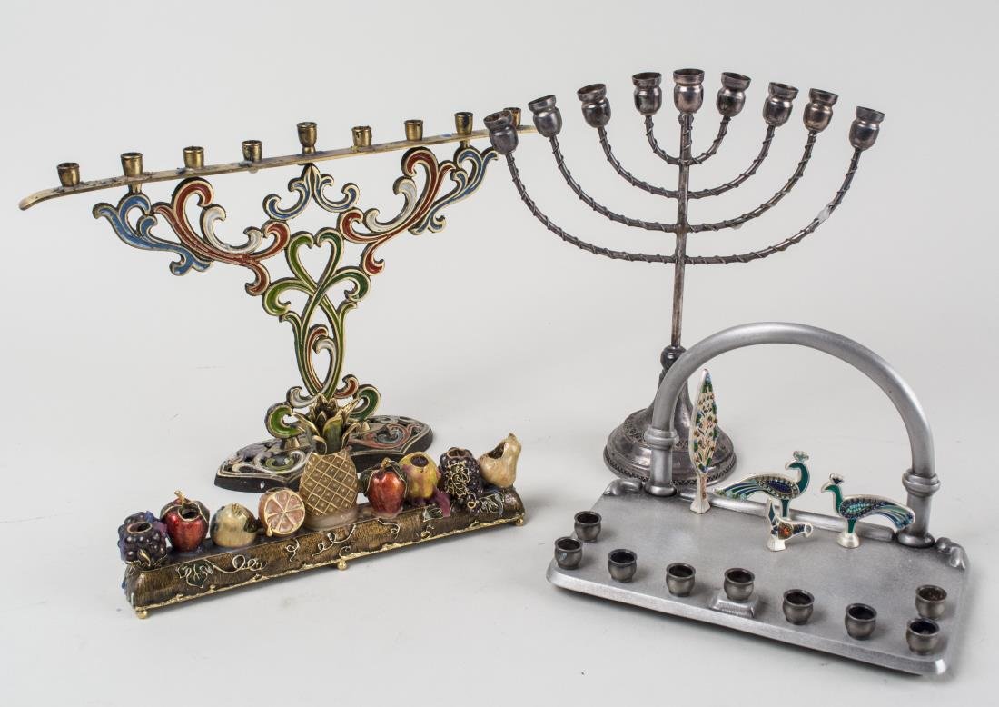 Group of Four Menorahs: Including one silver plated menorah, one brushed metal menorah with bird and tree decoration, one Jay Strongwater style menorah with fruit decoration, and one brass menorah with enamel decoration. Tal