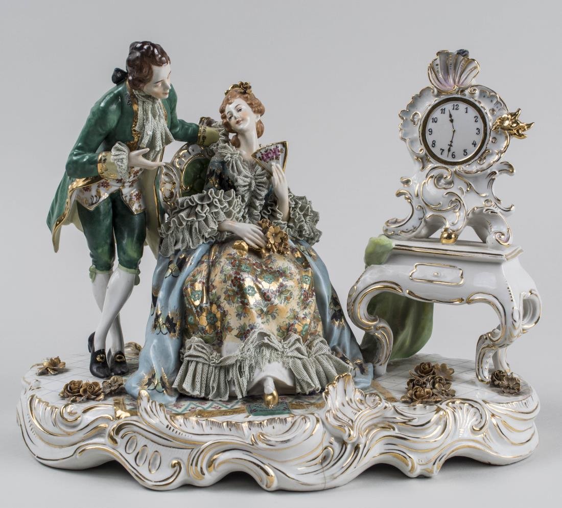 German Porcelain Figure Group: Depicting a courting couple, woman seated with a bouquet of flowers and holding a fan, next to a table with a clock, marked on the back. Height 11 inches. Notice to bidders: Condition reports and addi