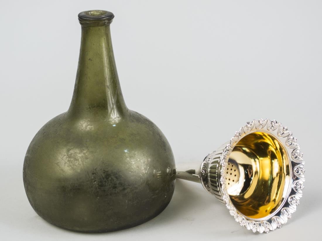 Glass Wine Bottle and Silver Plated Wine Funnel: Green glass bottle and a silver plated wine funnel. Bottle height 7 1/4 inches. Notice to bidders: Condition reports and additional photographs are provided by request as a courtesy to our clients, as