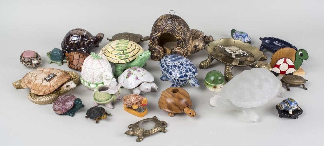 Group of Turtle Form Table Articles: Approximately twenty nine pieces, porcelain, glass, leather, composite, and brass examples, including trinket boxes, candle holders, trays, a coin bank and purse, a napkin holder, etc. Various sizes. 