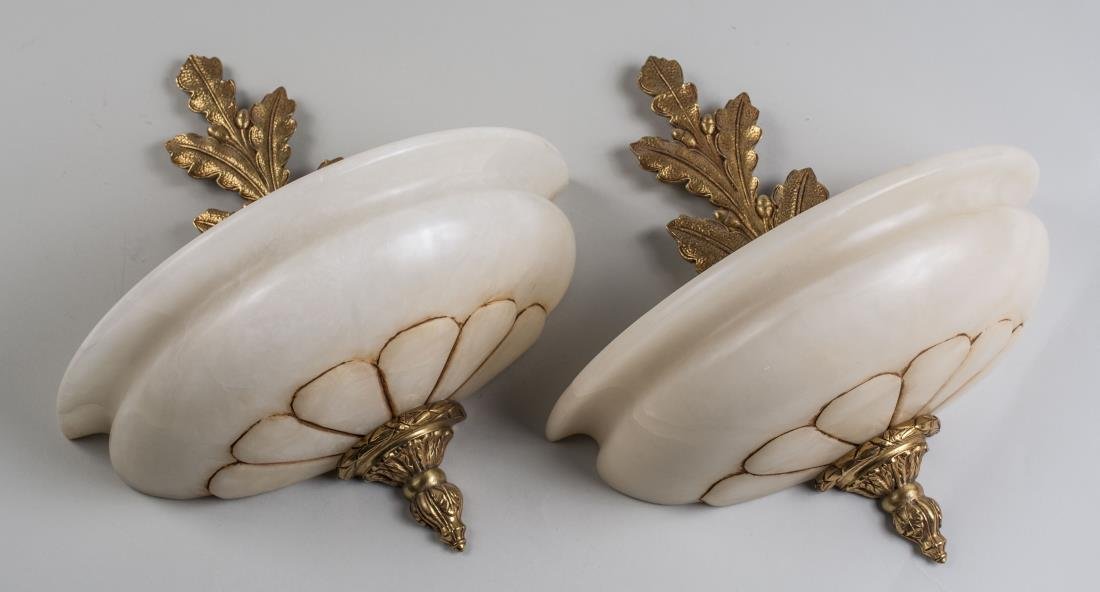Pair of Alabaster Wall Sconces: Bombe carved alabaster sconces with brass oak leaf trim. Height 14 inches. Notice to bidders: Condition reports and additional photographs are provided by request as a courtesy to our clients, as such