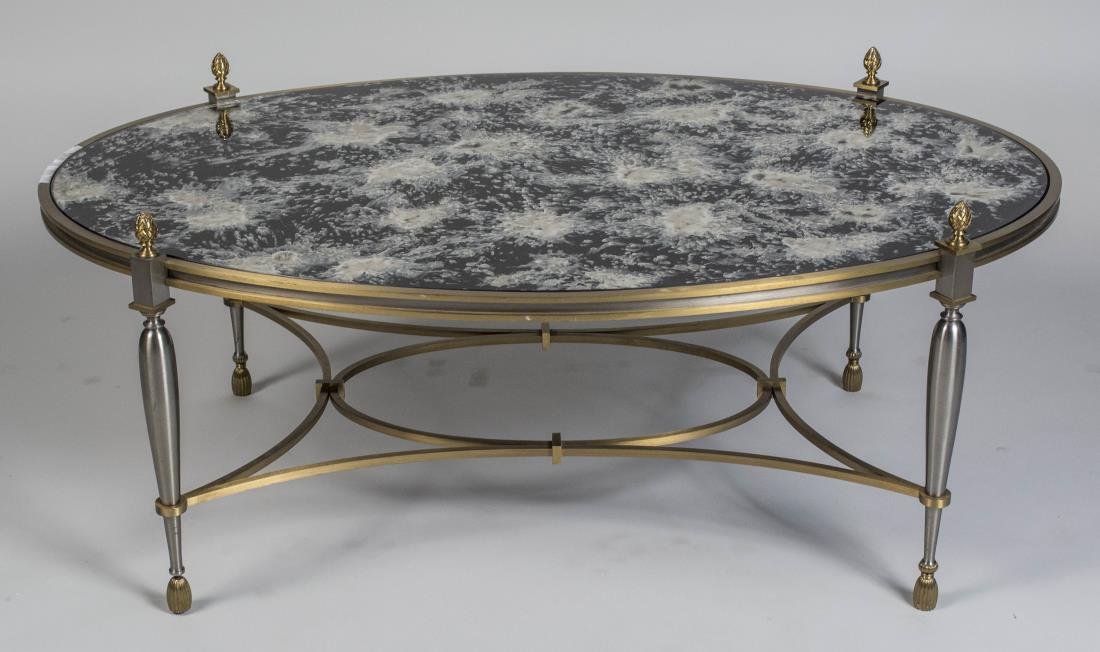 Brass and Brushed Metal Coffee Table: Oval mirrored top on a neoclassical style base with four inverted baluster form legs with acorn finial and joined by a modified box stretcher. Height 18 inches, width 43 inches, depth 28 inches. Notic