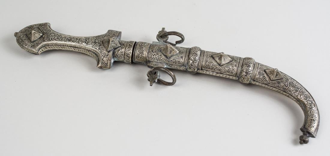 Jambiya Dagger: The double edged curved blade with with silvered metal and brass grip with stud and etched scroll decoration, with matching scabbard. Blade lenght 9 1/4 inches, overall 16 1/2 inches. Notice to bidder