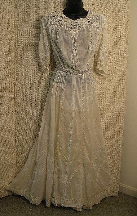 Victorian Lawn Dress Circa 1910: White cotton, scoop neck, net lace, inset embroidered medallions, pin tucked bodice/ 3/4 sleeves, MOP button back. Condition: Good, needs few seam repairs, small breaks at hemline, few light spots on 