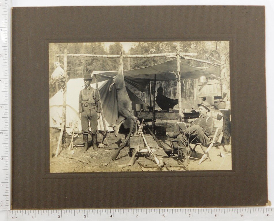 Photo of Deer Hunting Camp - Amity, Oregon: Image shows two men with Winchester and Savage rifles. One deer is shown hanging. Box rifles are leaning on is marked. Amity, Oregon. Photo is 7" x 5" mounted it is 7 7/8" x 10".