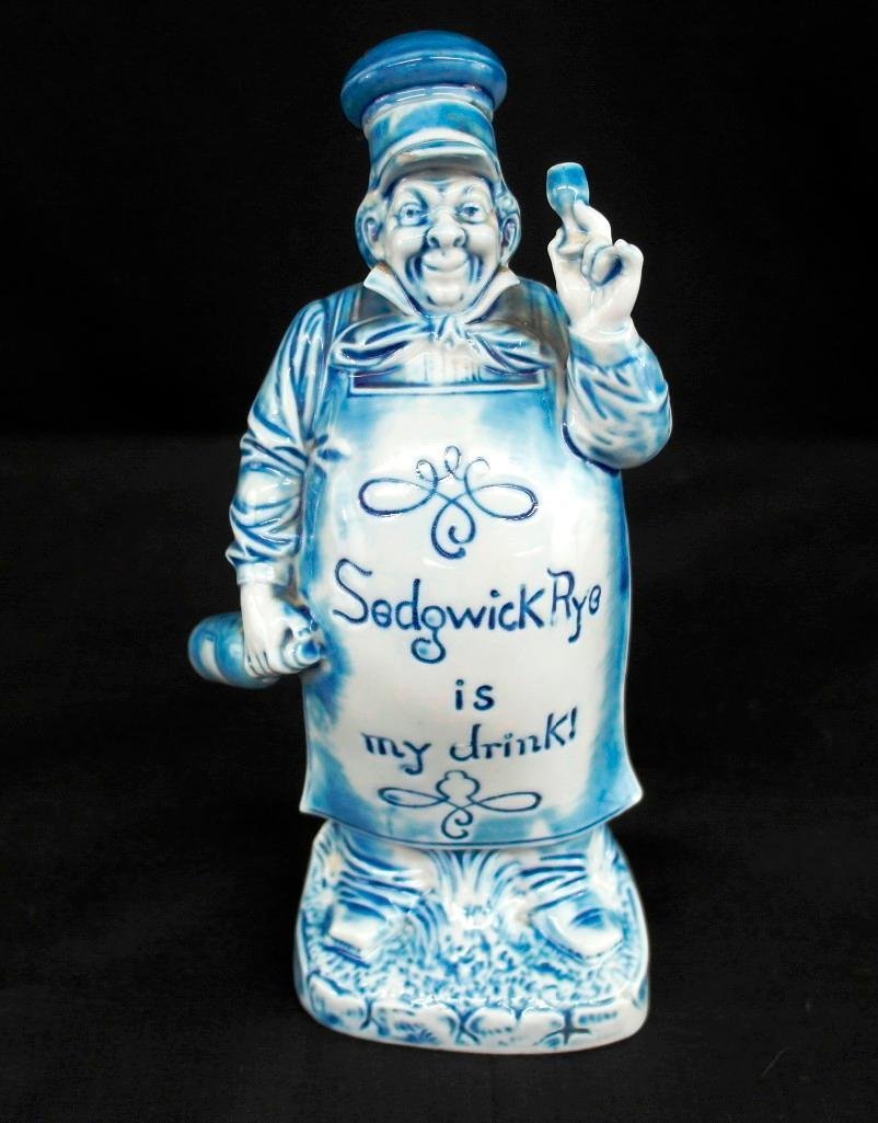 Schafer & Vater Figural Nipper - Blue Baker - "Sedgwick: This Schafer & Vater blue figural nipper is a baker with the inscription "Sedgwick Rye is my drink!" on the apron. This flask comes with the original stopper and measures approximately 8" tall. There