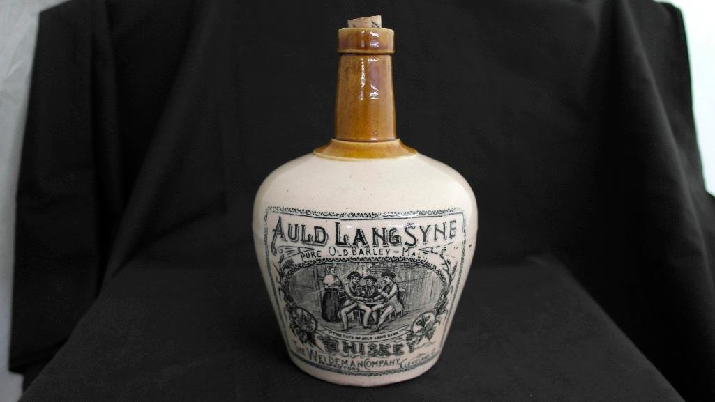 Pre-Prohibition Auld Lang Syne Whiskey Jug from: This lot is for a pre-prohibition era quart stoneware whiskey jug. It has a very detailed transfer label of a woman and three men sitting at a table drinking and surrounded by plants, company logo, et