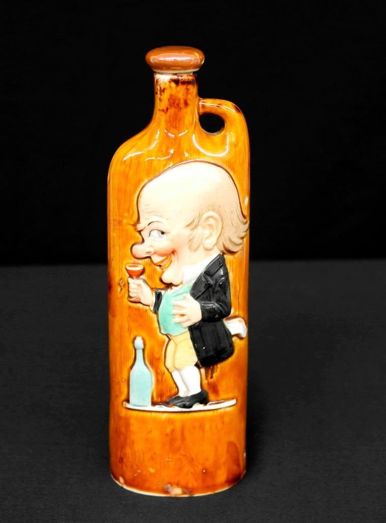 Schafer & Vater Colored Slim Flask "Bald Guy": This Schafer & Vater slim flask depicts a bald professional man sipping some type of spirits from a glass. There is no inscription near the bottom like on some flasks and he is referred to as Bald Guy