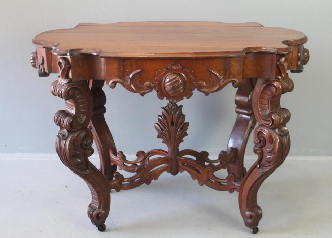Profusely Carved Mahogany Lamp Table: Profusely carved mahogany lamp table, fat cabriole legs sitting on original brass casters, pierce carved cross stretcher base with huge acanthus leaf pediment, turtle shaped top, (minor old seam separ