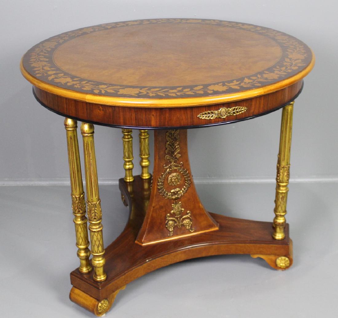 Contemporary Center Table: in burled wood veneers on 36" round top with border of marquetry inlaid flowers and leaves. Six gilded reeded carved posts support the edges with a canted column in the middle with applied ormolu, all