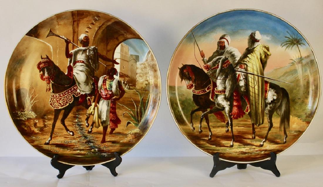 Pair Bernardaud & Co. Limoges Chargers: 19.25" diameter, each painted with Mid-East Orientalist scenes of men on horseback, each artist signed "Dusson", one has secondary signature "Cojou", artwork features raised enameling, truly a stunnin