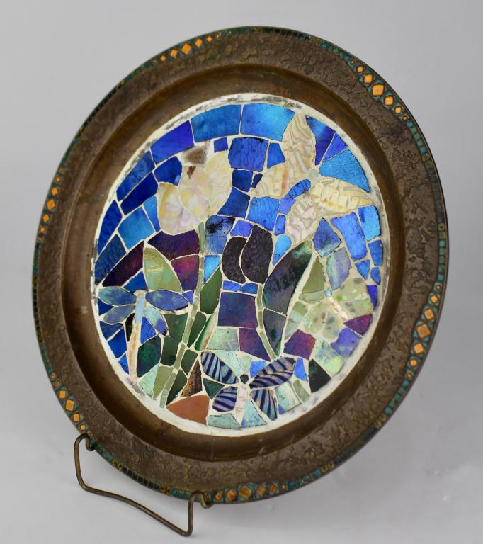 Rare Tiffany Furnaces, Inc. Bronze Plate: #304, mosaic glass interior with florals and butterflies, orange and green enameled rim, impressed signature and logo. 11.5" diameter, missing a tile shard in one spot, otherwise good condition.