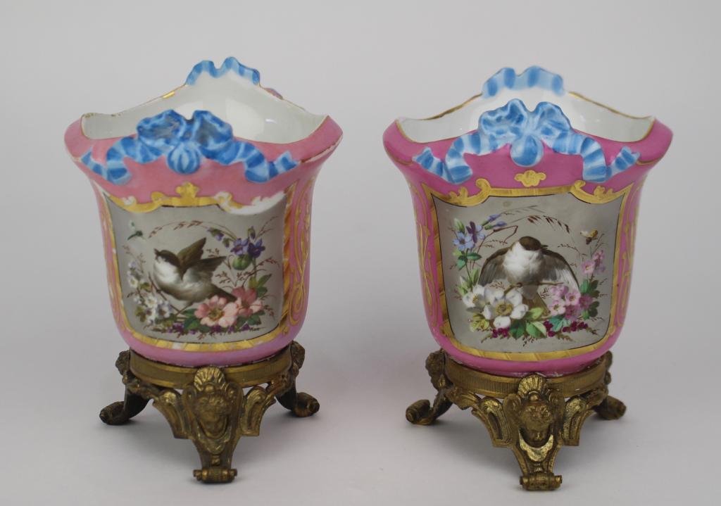 Pair Old Paris Petite Cache Pots: ornate footed bronze ormolu stands, each with hand painted panel scene of birds and florals, c. 1830. Pink body, gold outline with minor loss, otherwise good condition. 6" x 4.5".