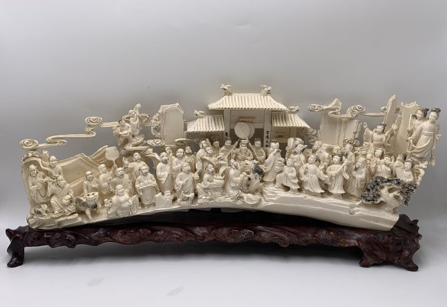 Chinese Hand Carved Bone Sculpture on Wooden Base: Chinese Hand Carved Bone Sculpture on Wooden Base. The hand carved sculpture depicts a gathering or celebration scene. The sculpture measures 25" tall x 8" wide x 6" depth. The wooden base measures 2"