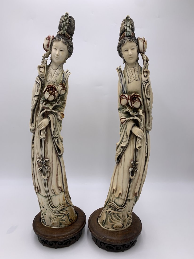 Pair of Chinese Hand Carved Bone Sculpture of Kuan-yin on Wooden Base: Pair of Chinese hand carved Sculptures of Kuan-yin in traditional robe holding flowers on a wooden base. The hand carved figures measures 18" tall x 4 1/2" wide x 2 1/2" depth. Makers mark on the bott