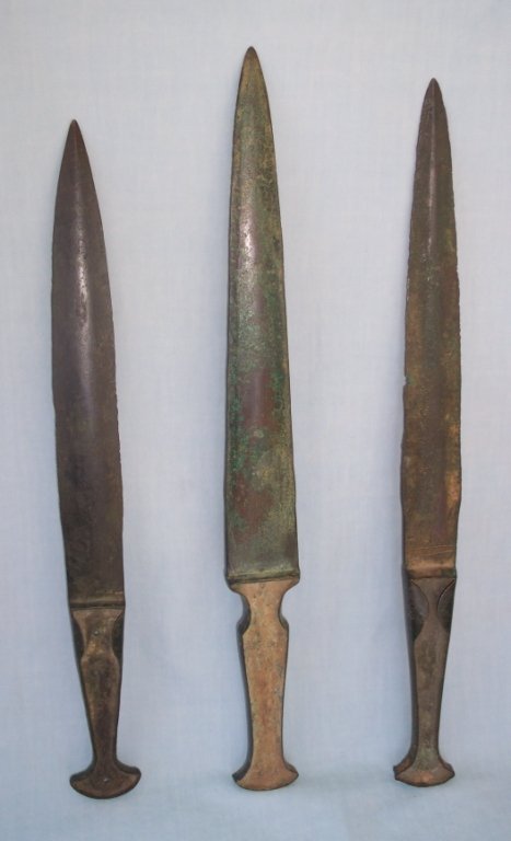 3 Bronze Age Daggers: 3 Bronze Age daggers or edged weapons, each forged bronze with excellent green/brown patina, one with Cherron band incised decoration, longest 10.5" with 5" grips, wood inserts long gone, from Lurista