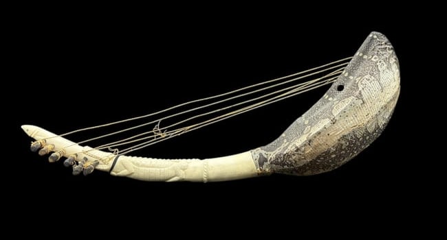 20th Century African Harp with Carved Alligator Figure Neck and Snakeskin Soundbox: 20th Century African Harp with Carved Alligator Figure Neck and Snakeskin Soundbox. The neck of the harp made by craftsmen in Africa shows an alligator with a fish in his mouth. The gourd shaped sound