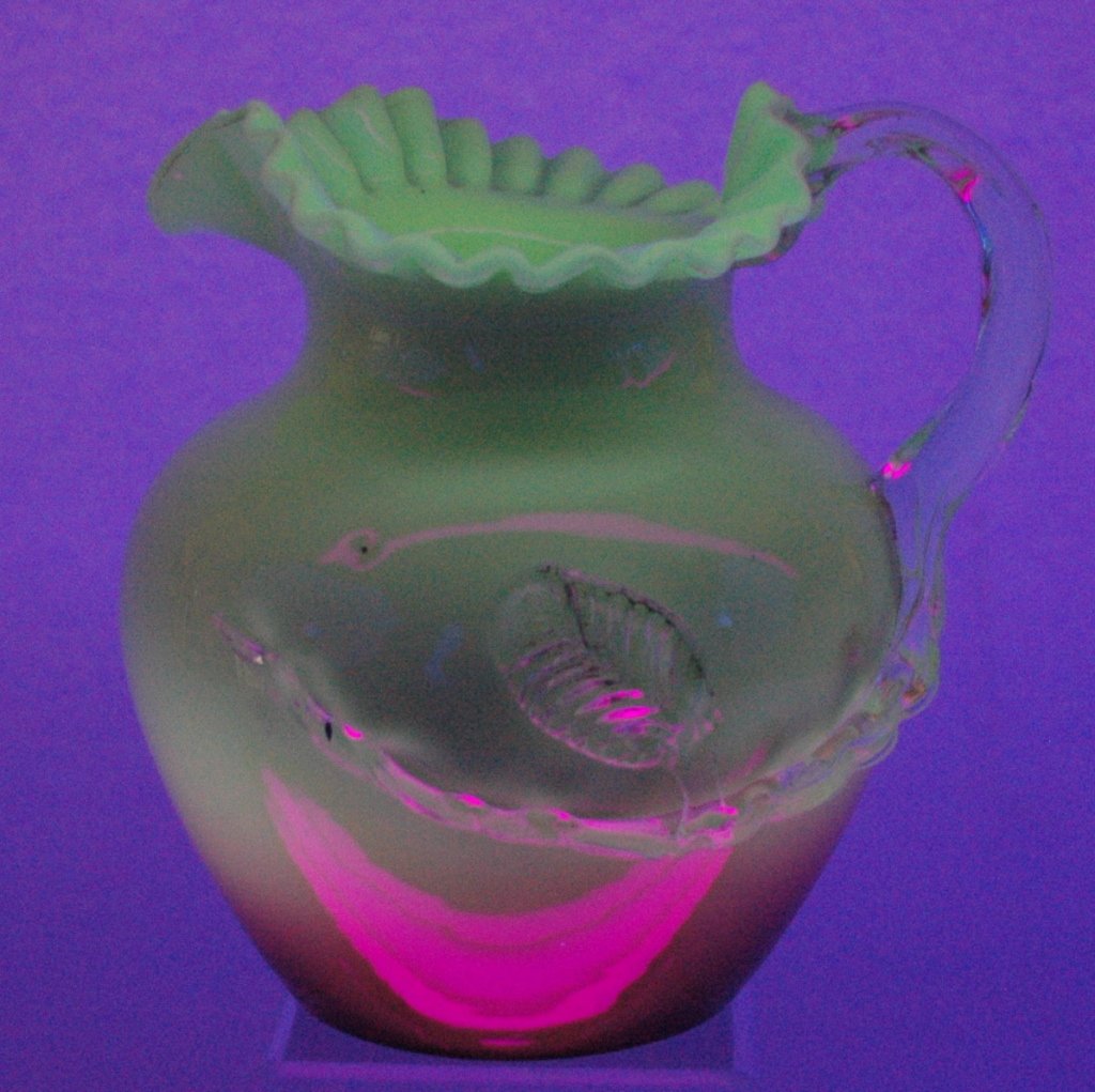 Glossy Peach Blow Pitcher: Glossy Peach Blow pitcher with applied clear handle and vine with leaf, ruffled top, maker could be Wheeling or Stevens & Williams. Also pictured under black light influence. 7" x 8" wide, good condit