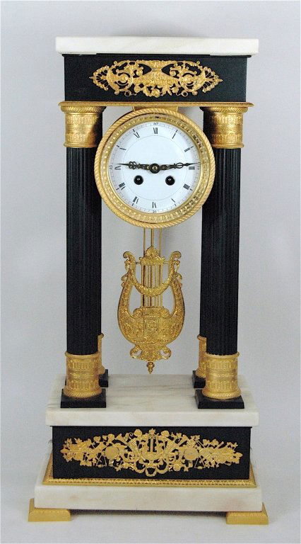 French Empire Clock: French Empire clock with 4 ebony columns, top and base, white marble top and base with ormolu mountings, white porcelain face. Lyre shaped pendulum, stunning. Time and chime. Unsigned. 24H, 13W.