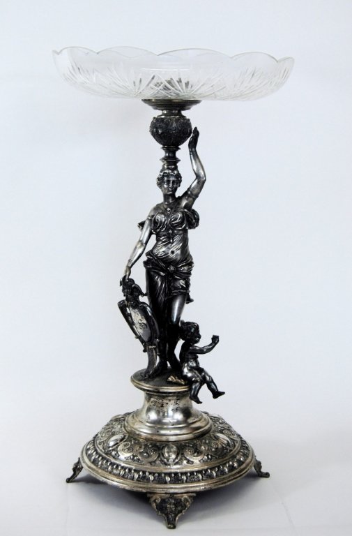W. M. F. Figural Tazza: fine silver plated figural tazza with Greek Goddess holding shield balancing cut glass bowl with putti at feet. All on multi-layer footed plinth. Very good condition, impressed mark, 23H, 12D.