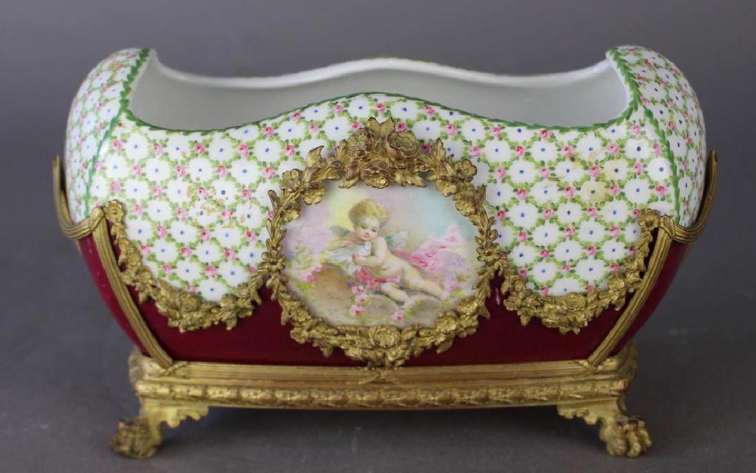 French Porcelain Fernier with Custom Stand: French porcelain fernier in ornate bronze ormolu holder, bowl features hand painted center medallion depicting putti with white dove, and en verso. Unsigned, 6" x 10" x 6", good condition.