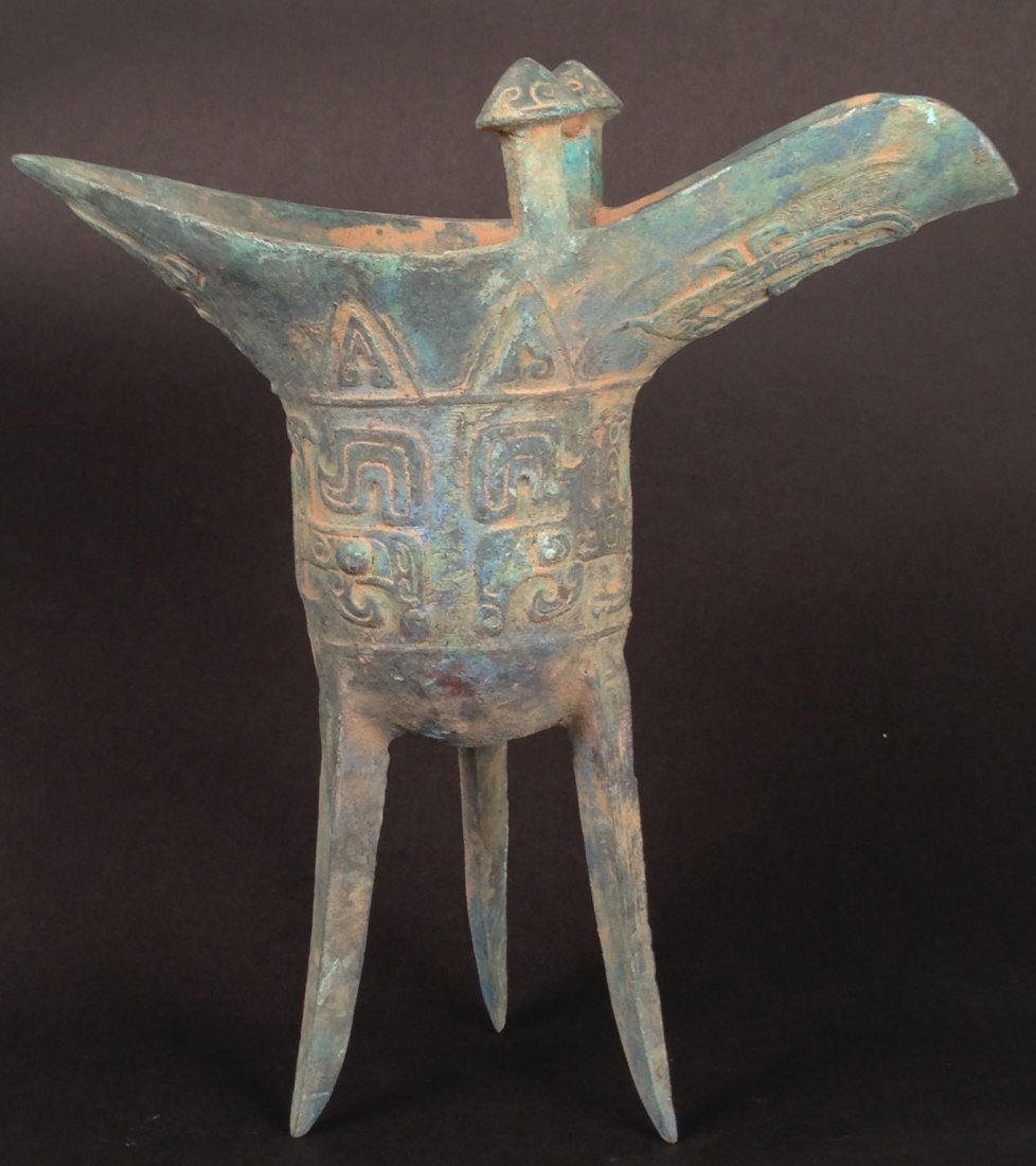 Chinese Bronze Wine Cup: bronze cup, Zhou dynasty, china, decorated with carved Taotie pattern on body and dragon shaped holder with three legs 9 x 9 Auction Estimate 1000-2000